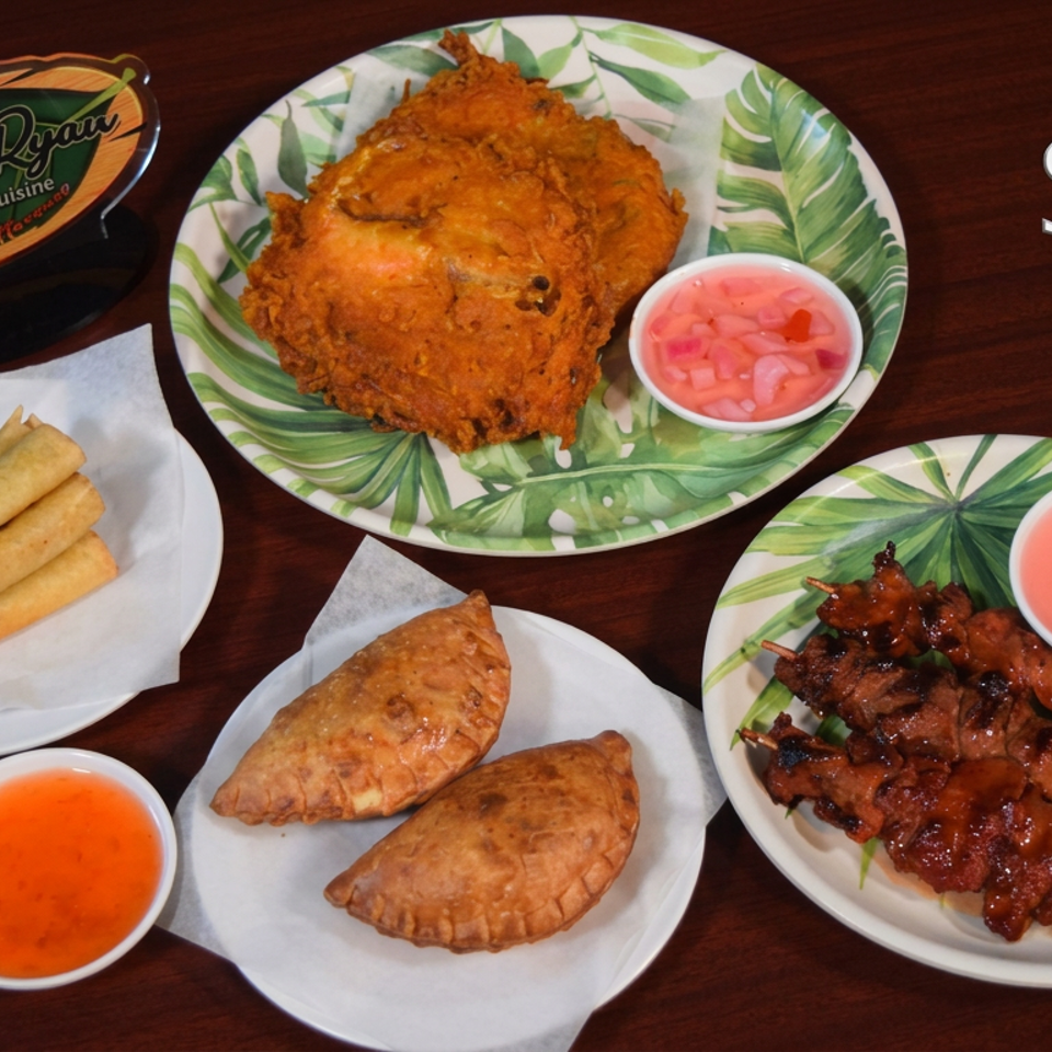 Filipino side dishes featuring fried chicken, spring rolls, empanadas, grilled skewers, and dipping sauces on a wooden table.